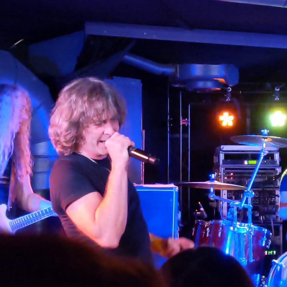 A man singing into a microphone on stage with a drum set.
